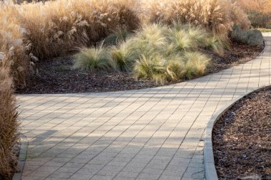 Çimlerin arasında kıvrılan taşla döşenmiş bir patika. Doğal ortam, insan tasarımı ile peyzajı harmanlıyor, sakin ve manzaralı bir yol sunuyor yürümek için mükemmel.
