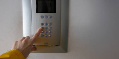 Bir insan eli bir apartmanın girişindeki tuş takımının tuşlarına basar. Erişim kontrol sistemi kişisel kod üzerinden güvenli giriş için kullanılır