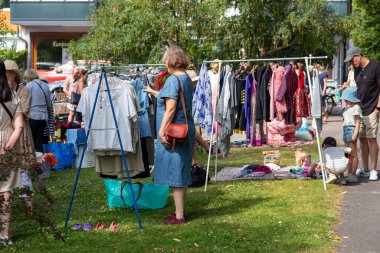 Hanko, Finlandiya - 31 Temmuz 2025: Finlandiya 'da kirppis veya loppis adında bir bit pazarında gezinen alıcılar, kullanılmış antika eşyalar ve satılık giysilerle dolu masalar. Tekrar kullan, ikinci el ve eko tüketici