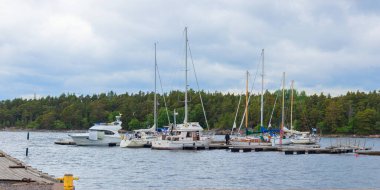 Jussaro, Ekenas, Raseborg, Finlandiya - 25 Haziran 2025: Jussaro adasının yelkenlileri ve motorlu tekneleri olan küçük tekne marinası, rıhtıma demirlemiş ve şamandıralara veya iskele, pankarta bağlanmış