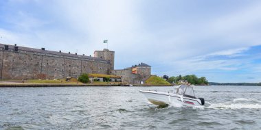 Tarihi Vaxholm Kalesi su ve yemyeşil ile çevrili, duvarları üzerinde gururla dalgalanan İsveç bayrağı, zengin miras ve manzaralı kıyı konumu ile