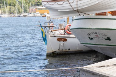 Stockholm, İsveç - 9 Temmuz 2025: Güneşli bir yaz gününde Stockholm şehrinin arka planında rıhtımda demirlemiş ahşap tarihi teknelerin manzarası
