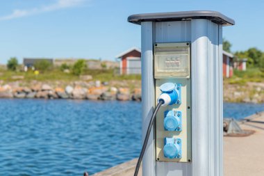 Finlandiya 'da bir yat limanındaki teknelerin şarj istasyonu, Baltık Denizi kıyısında limana demirli iken, yelkenlilerin ve motorlu teknelerin şarj edildiği elektrik prizleriyle dolu.