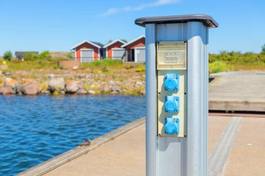Finlandiya 'da bir marina iskelesinde tekneler için şarj istasyonu. Deniz kıyısında güneşli bir yaz günü kıyıya yanaşan yelkenli ve motorlu tekne elektrik prizleri.