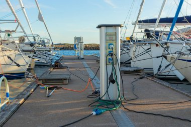 Finlandiya 'da bir yat limanındaki teknelerin şarj istasyonu, Baltık Denizi kıyısında limana demirli iken, yelkenlilerin ve motorlu teknelerin şarj edildiği elektrik prizleriyle dolu.
