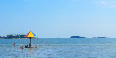 Finlandiya 'nın Hanko plajında deniz kenarındaki renkli bir atlıkarınca. Yetişkinler ve çocuklar güneşli bir yaz gününde deniz kenarındaki eğlence merkezinde eğleniyor.