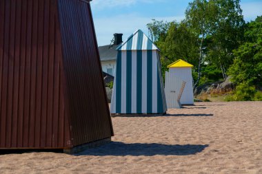 Finlandiya 'nın Hanko şehrindeki güneşli kumlu plajlarda renkli ikonik kulübeler, kulübeler, kulübeler, neşeli bir Fin Riviera havası ve deniz manzaralı deniz kenarı tatil köyü atmosferi bulunmaktadır.