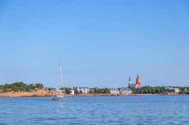 Deniz kenarındaki Hanko şehrinin panoramik manzarasında tarihi kırmızı su kulesi, Lüteryen Katedrali, yelkenlisi, kıyı yaşamı ve mimari simgeleri yer alıyor.