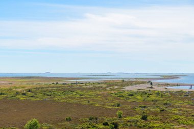 Finlandiya 'daki Jurmo Adası' nın çorak ve düz manzarası, düşük büyüyen bitkilerle kaplı açık bir gökyüzünün altında uzanır. Bu eşsiz İskandinav manzarası dayanıklılık, izolasyon ve kırılgan ada ekolojisini yansıtır.