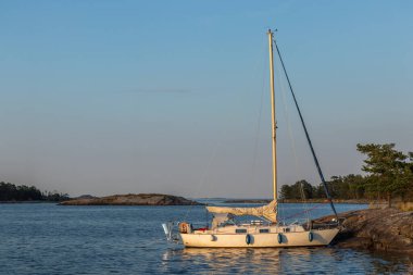 Kıyıdaki kayalıklara demirlemiş küçük yelkenli sakin sularda dinleniyor. Kırsal deniz hayatı, Fin doğasıyla yakın ilişki, Baltık Denizi kıyısında huzurlu anlar