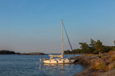 Kıyıdaki kayalıklara demirlemiş küçük yelkenli sakin sularda dinleniyor. Kırsal deniz hayatı, Fin doğasıyla yakın ilişki, Baltık Denizi kıyısında huzurlu anlar