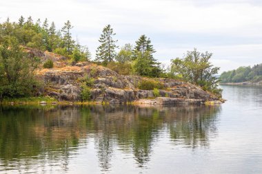 Güneş ışığında Baltık Denizi kıyısında dik kayalık bir uçurum. Engebeli taş dokular, parlak kuzey ışığı, dramatik kıyı manzarası ve Fin deniz manzarası.