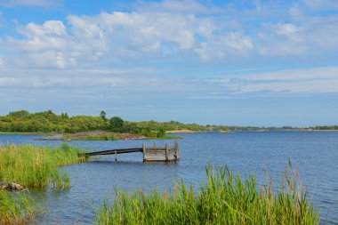 Baltık sularına uzanan ahşap duba ile güzel bir deniz manzarası. Barışçıl İskandinav kıyı manzarası uyumu, rahatlığı ve çevre dostu yolculuğu sembolize eder.