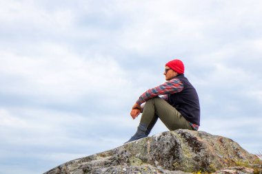 Genç adam Fin doğasında yürüyüş sırasında oturur ve dinlenir. Açık hava macerası, rahatlama ve kuzey vahşi doğayla bağlantıyı vurgular