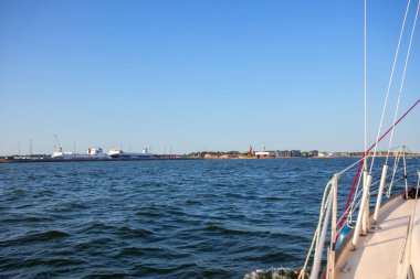 Finlandiya, Hanko - 17 Temmuz 2025: Uzak Hanko kenti ile birlikte ufka doğru yelkenli bir yatın pruvasından bakın. Deniz macerası, seyahat ve deniz ve şehir manzarası arasındaki bağlantı
