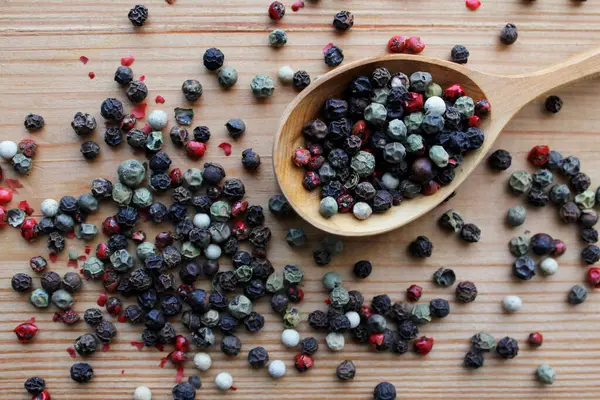 Beyaz ahşap arka planda ahşap kepçeyle siyah biber.