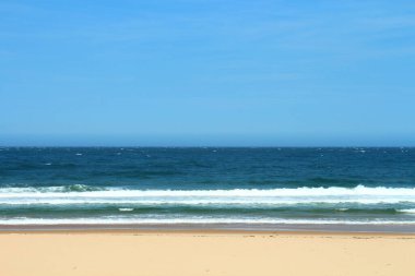 Güneşli bir yaz gününde mavi okyanusun dalgalarının tadını çıkaran insanlarla dolu kalabalık bir kumsal..