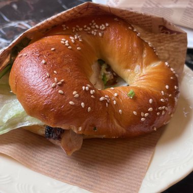 Taze yapılmış bir simit sandviçi bir tabakta oturur, parlak, altın rengi bir dış serpilmiş susam tohumlarıyla sergilenir. Marul ve et gibi malzemeler içerir, keyif verir..