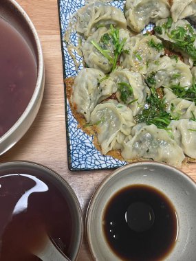 A vibrant selection of dumplings lies on a decorative plate alongside bowls of rich dipping sauces and warm soup. This inviting meal showcases fresh ingredients and flavors. clipart