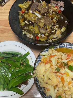 Tahta bir yüzey üzerinde üç farklı yemeğin canlı görüntüsü. Bir kasede soslu sığır eti ve sebzeler yer alırken, diğerlerinde kızarmış yeşiller ve renkli bir sebze karışımı sergileniyor..