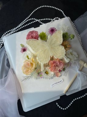 A stunning cake is adorned with a large butterfly made of white icing and surrounded by delicate flowers. It is set on a dark backdrop, perfect for a festive occasion. clipart