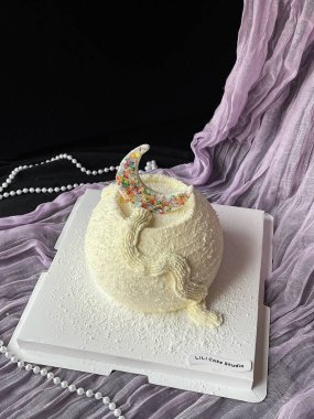 Çok güzel hazırlanmış bir pasta vitrinleri pürüzsüz beyaz bir dış görünüş, üzerinde renkli bir hilal dekoru var. İnciler ve yumuşak kumaş, kutlama için mükemmel bir sunum sunar..