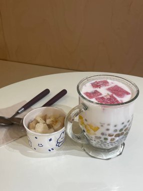 Renkli jöle, meyve ve hindistan cevizi sütüyle dolu küçük bir bardak taze muz dilimlerinin eşlik ettiği rahat bir kafede lezzetli bir tatlı servis edilir..