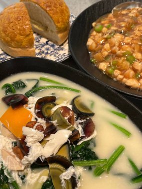 Canlı Asya yemekleri, sebzeli bir kase deniz ürünleri çorbası, kızarmış tavuk yemeği ve taze ekmek ruloları sergiler. Baştan çıkarıcı renkler ve dokular tatmin edici bir yemek deneyimi vaat ediyor..