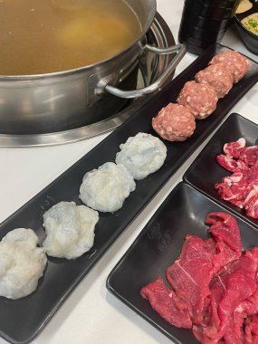 Bir yemek masası, köfte, köfte ve ince dilimlenmiş et de dahil olmak üzere çeşitli taze malzemelerle lezzetli et suyunda pişirilmeye hazırdır..