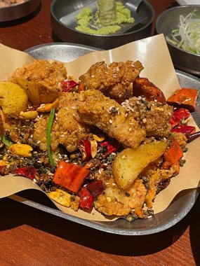 Kızarmış tavuk parçaları renkli sebzeler ve aromatik baharatlarla bir tabağa konur. Yemek susam tohumları ve biberlerle süslenmiş, canlı dokular sergileniyor..