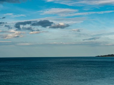 Mavi gökyüzünde güzel bulutların olduğu sakin mavi deniz manzarası huzur verici ve rahatlatıcı bir atmosfer yaratır..