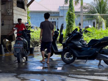Aceh, Endonezya - 26 Eylül 2024: Ahşap bir yer olan Acehnese toplumuna ait geleneksel bir koğuşta motosiklet yıkayan bir işçi