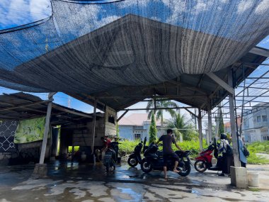 Aceh, Endonezya - 26 Eylül 2024: Ahşap bir yer olan Acehnese toplumuna ait geleneksel bir koğuşta motosiklet yıkayan bir işçi