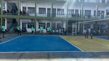 Aceh, Endonezya - 14 Haziran 2023: Bir grup voleybol oyuncusu sarı ve mavi voleybol sahasında, seyirciler maçı izliyor.