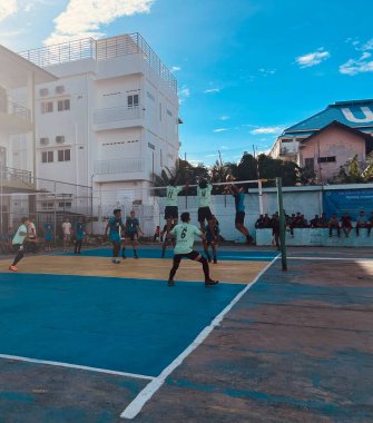 Aceh, Endonezya - 14 Haziran 2023: Bir grup voleybol oyuncusu sarı ve mavi voleybol sahasında, seyirciler maçı izliyor.