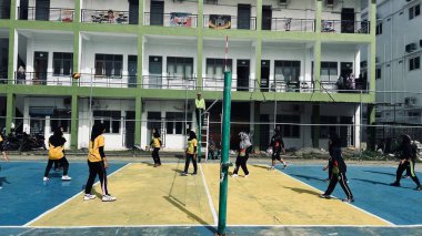 Aceh, Endonezya - 14 Haziran 2023: Bir grup voleybol oyuncusu sarı ve mavi voleybol sahasında, seyirciler maçı izliyor.
