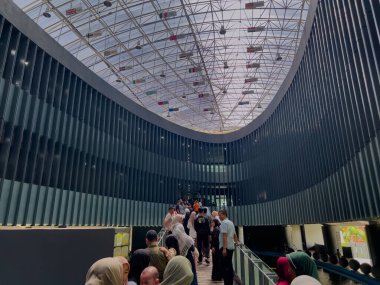 Aceh, Indonesia - May 14, 2024: Tourists standing on the pedestrian bridge inside the Aceh Tsunami Museum, with the museum's roof adorned with various hanging national flags. clipart