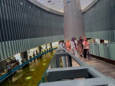 Aceh, Endonezya - 14 Mayıs 2024: Müzenin çatısı çeşitli ulusal bayraklarla süslenmiş Aceh Tsunami Müzesi içindeki yaya köprüsünde duran turistler.