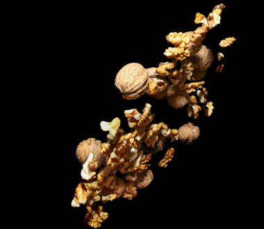 Birçok ceviz, siyah arka planda izole bir şekilde havaya atıldı. Dar odaklı. Kırılmamış fındık ve kırılmış fındık karışımı..