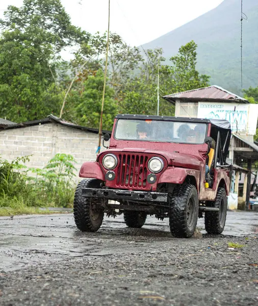 Kırmızı Jeep Çamurlu Yol 'da Volkan Arkaplanda Sürüyor