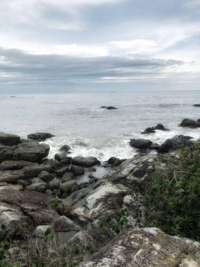 Mavi gökyüzü, gri bulutlar, açık deniz, Akdeniz kayaları, bazı dalgalar ve ormanlar.