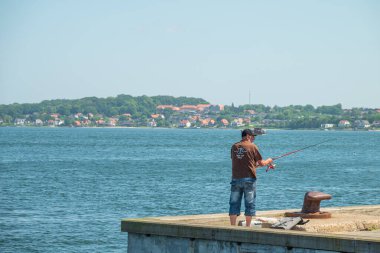 Middelfart, Danimarka - 2 Haziran. 2024: İskelede balık tutan adam