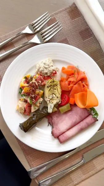 Bu eko-gastronomi deneyiminde sosisli sandviç, enginar, tavuk salatası ve somon ilgi odağı oluyor. Sofistike bir otel yemeği, beyaz tabakta zarif bir şekilde servis ediliyor. Otel yemeği için lüks bir seçenek.