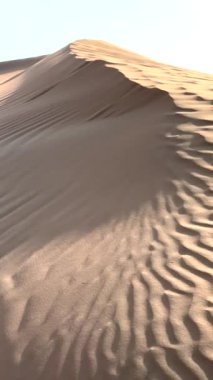 Akşam çöle düşer, yumuşak turuncu kumullar, pembe renkler. Kum kıvrımları solan ışıkta göze çarpar, sakin çöl manzarasının sakin güzelliğini yakalayarak, gündüzleri geceye dönüşürken..