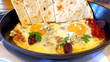 Zeytin yağı ve pita ekmeğiyle aromalı haşlanmış domates soslu haşlanmış yumurta güne lüks bir başlangıç sunar. Tabak, doğal malzemelerin basitliğiyle temiz yemek karmaşıklığını birleştirir.