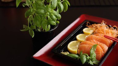 Kırmızı tabak, restoranda sashimi sunumunu geliştirir. Fesleğen ve limonla taze balık dilimleri gelişmişlik için özel kırmızı çubuklarla eşleştirilmiş görsel olarak çarpıcı bir yemek oluşturur..