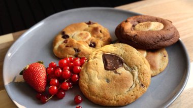 Gri tabakta bisküviler taze böğürtlenler ve sıcak bir fincan çayla basit bir rahatlatıcı kahvaltı sunar. Bu ortam, sadeliğin güzelliğini takdir edenler için rahat ve rahat bir sabah atmosferini somutlaştırır.