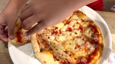 Childs 'ın elleriyle dilimlenmiş büyük, taze pişmiş bir pizza. Sahne, pizzanın karşı konulamaz çekiciliğinin altını çiziyor. Çocuklar zevkten dört köşe oluyor..