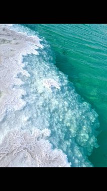 Kristalize edilmiş tuz oluşumu berrak suya karışıyor, dokulu beyaz tuz ve şeffaf turkuaz su arasında dinamik bir etkileşim yaratarak doğal elementlerdeki uyumu vurguluyor. Dikey fotoğraf