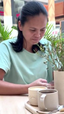 Abu Dhabi, BAE - 17 Eylül 2024: Çağdaş alanda kahve molası sırasında telefonu kontrol eden hemşire, yeşil ve barışçıl bir ortamla çevrili, zihinsel şarj sunan gevşemeyi teşvik ediyor 